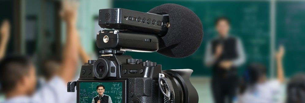A video camera recording a teacher standing in front of a blackboard.